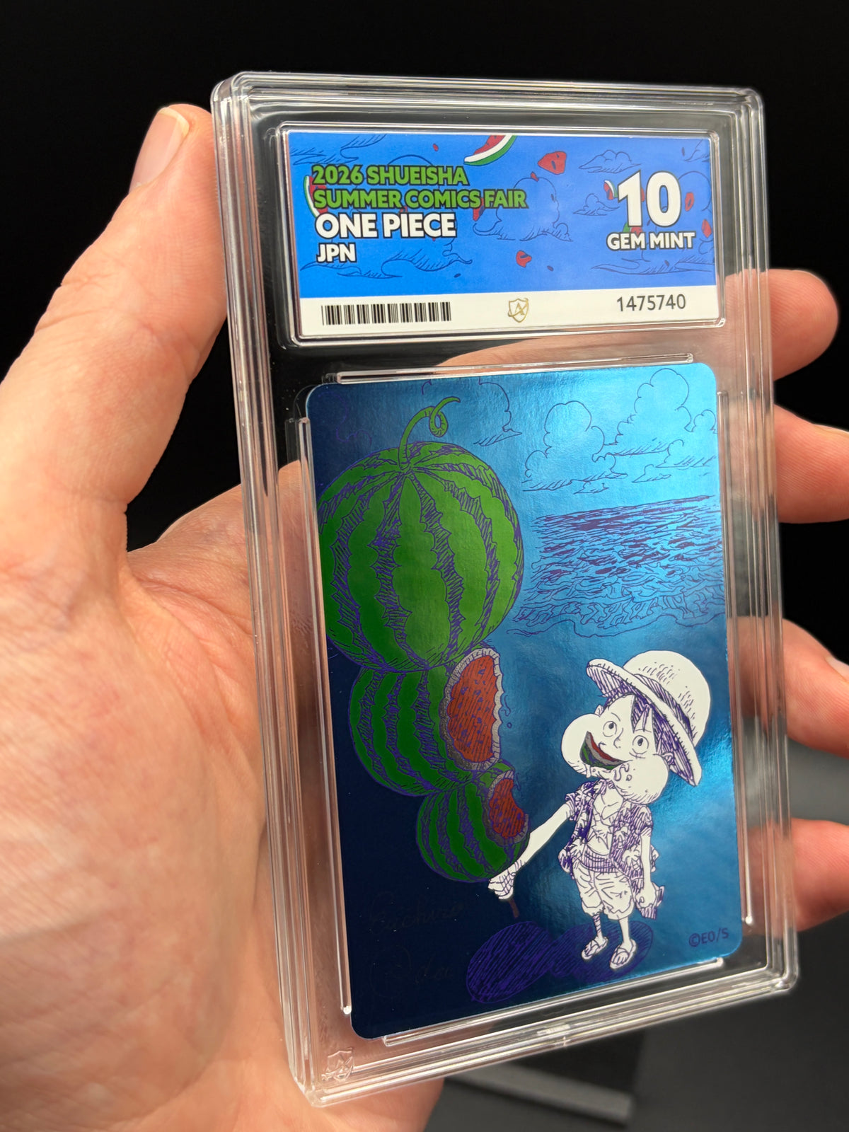 Handheld close-up of Watermelon Luffy One Piece Shueisha Summer Comics Fair 2026 Japanese promo in an ACE 10 Gem Mint slab, showing blue foil artwork