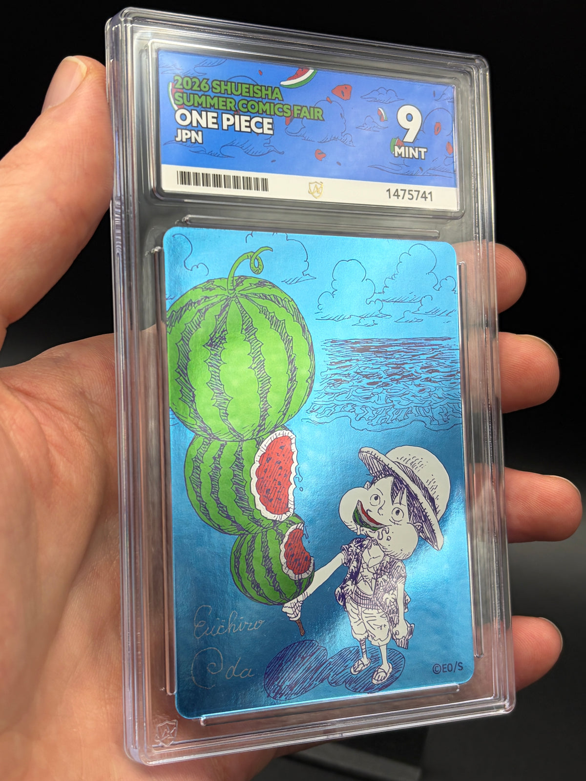 Handheld close-up of Watermelon Luffy One Piece Shueisha Summer Comics Fair 2026 Japanese promo in an ACE 9 Mint slab, showing blue foil artwork